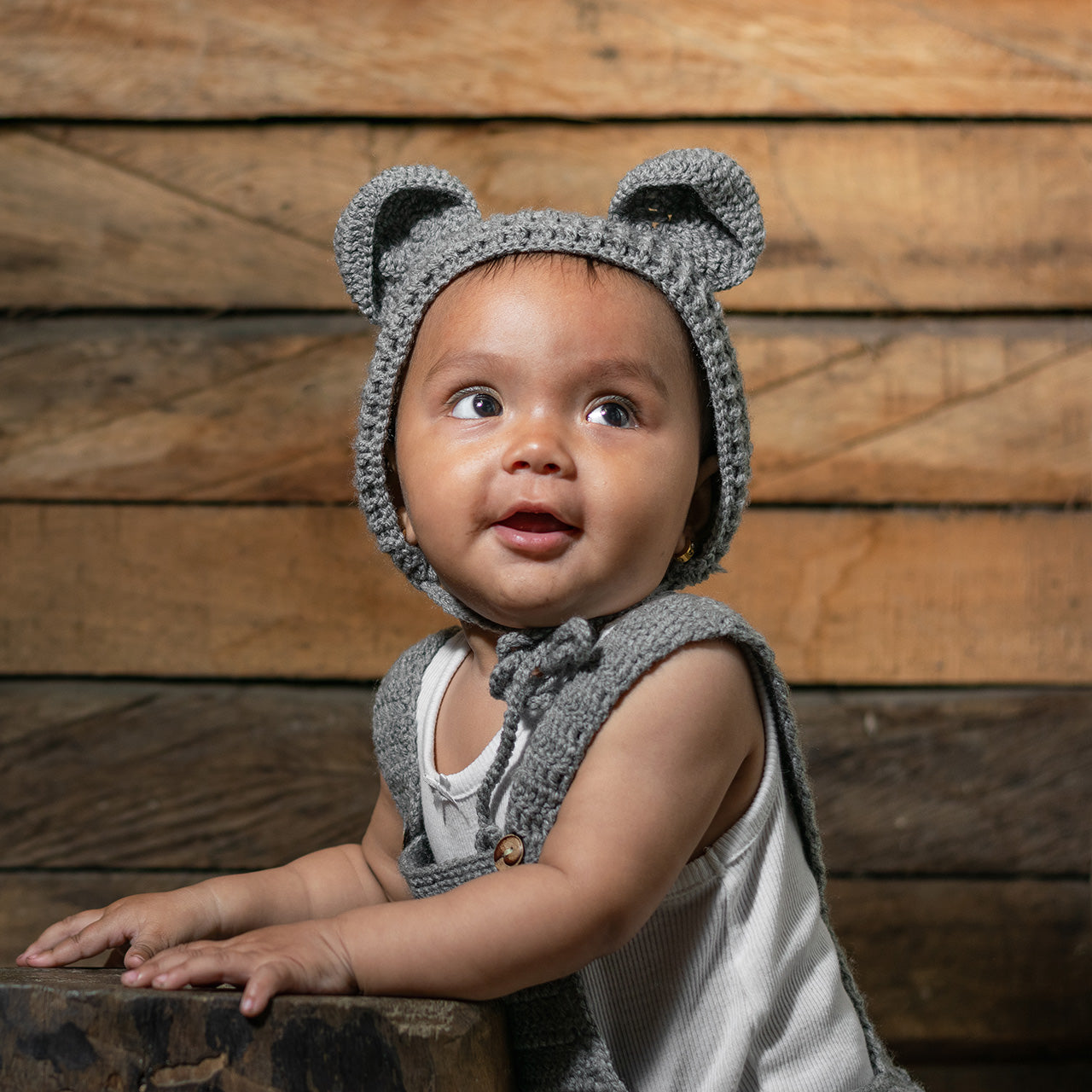 Baby with brown skin wearing overalls and a cap