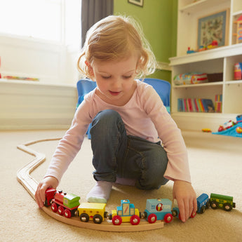 Girl toddler playing with train track toys in the playroom